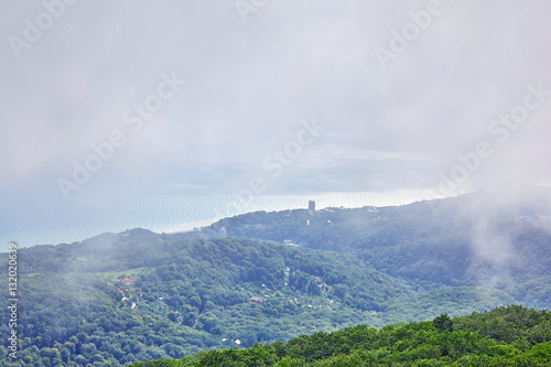 reen hills in valley with low grey clouds and mist on the Black Sea coast with wavy far water surface reflecting sun light  © boligolovag