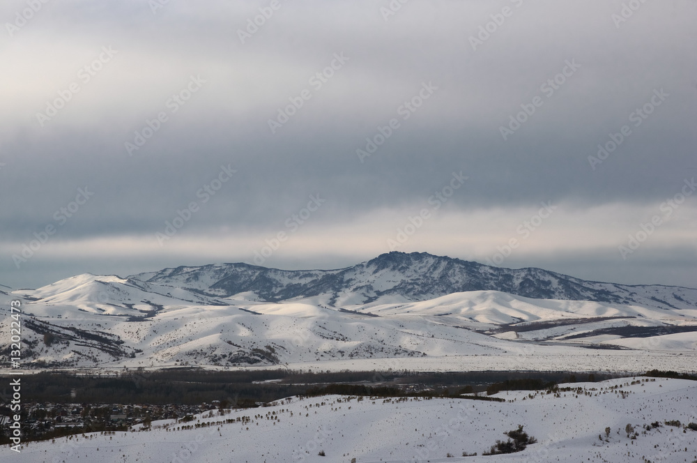 Winter snow mountain valley with rocky hills under cloudy gloom sky. Altai Mountains, Siberia, Russia