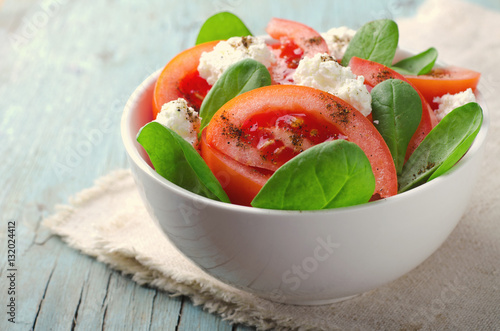 Tomato salad with spinach, cottage cheese, olive oil and pepper on blue wooden background