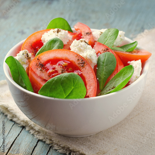Tomato salad with spinach, cottage cheese, olive oil and pepper on blue wooden background