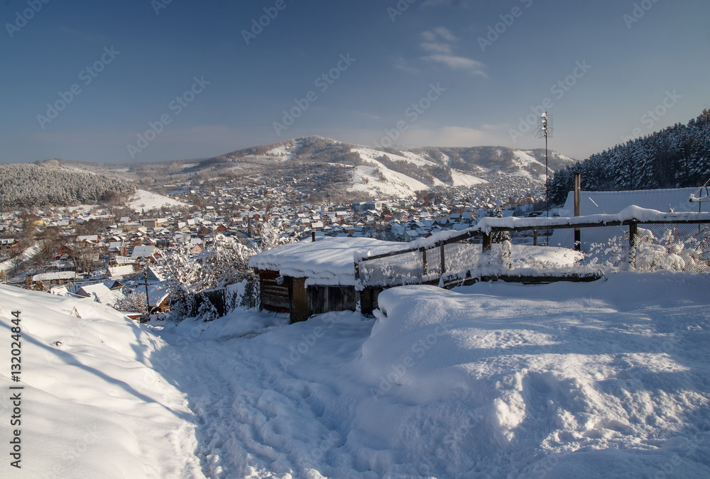 Winter snowy mountain valley with village town and ranges of snow hills on the background under blue sky Altai Mountains, Siberia, Russia