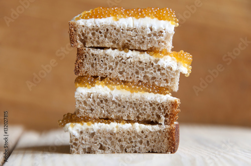Quadro em tela Multilayer sandwich of bread, cream cheese and pike caviar close-up on light wood surface