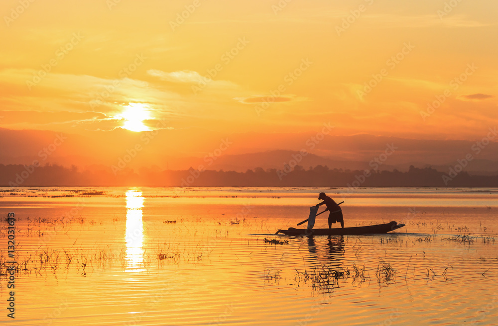 Silhouette of fisherman on wooden boat in nature lake with sunrise