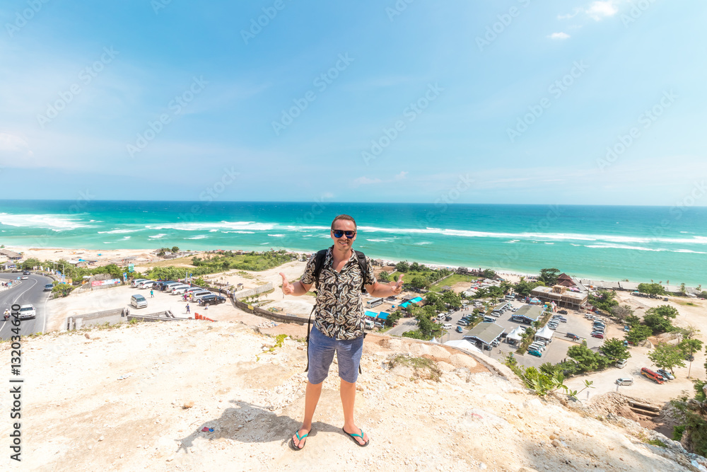 Handsome traveler man stay by blue ocean background - Happy guy relaxing at sea view point - Concept of freedom and summer trip around the world backpacker style. Bali, Indonesia.