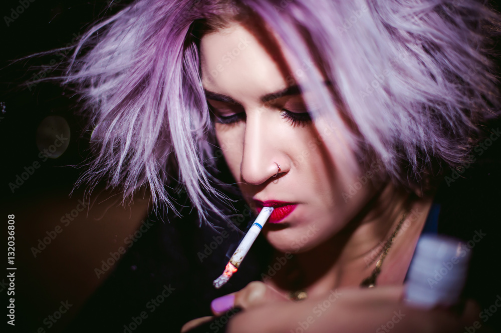 Obraz premium Portrait of a girl with a cigarette. young beautiful girl hipster smoking a cigarette in the street under the snow. her hands lights a lighter, lighting a cigarette tobacco