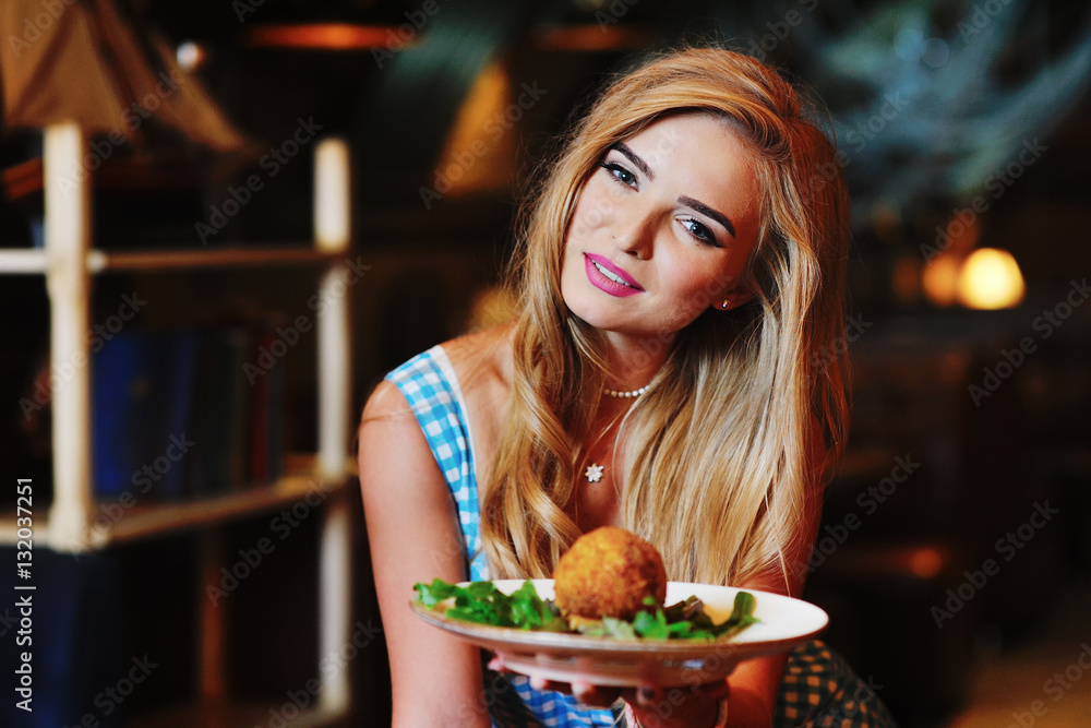 attractive woman in blue sundress offers delicious meat cutlet ball on the background of the restaurant