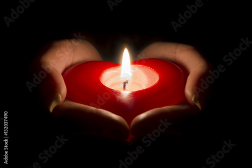 woman's hands holding a heart shaped candle in the dark