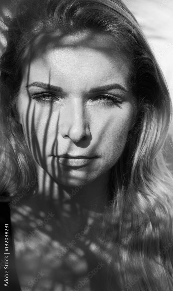 Black and white portrait photo of pretty blonde woman with palm tree leaves pattern shadow on her face and body
