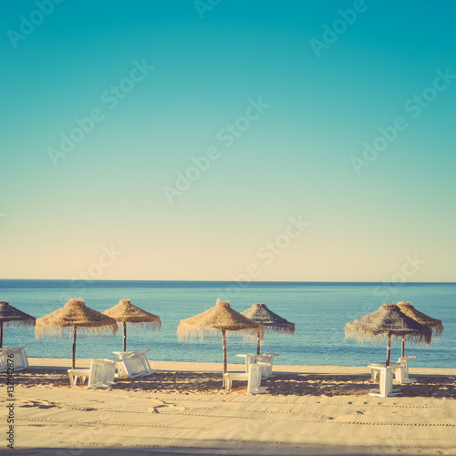 Holiday and vocation image with sandy beach, parasol and chairs on outdoors background