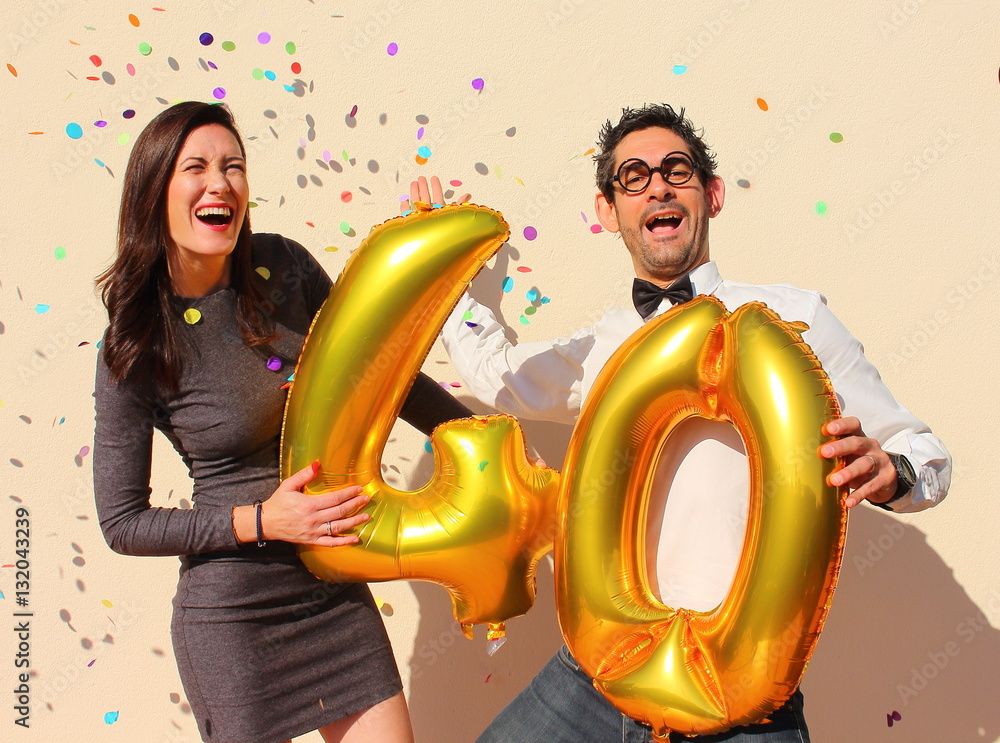 Φωτογραφία Cheerful couple celebrates a forty years birthday with big golden balloons and colorful little pieces of paper in the air