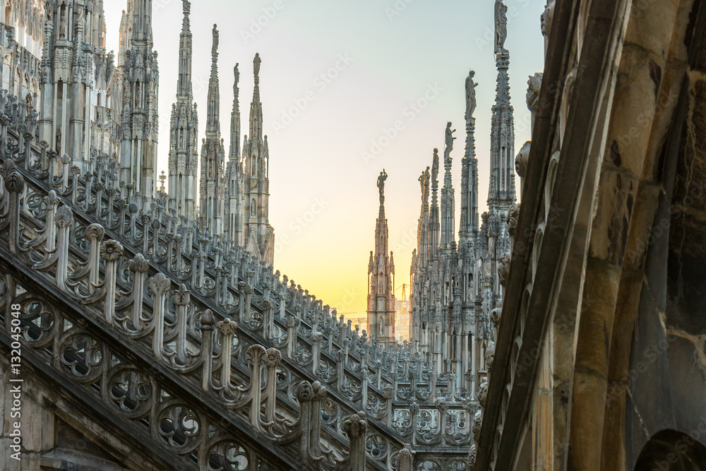 Details of marble spiers and statues of Milan Cathedral, Italy, at sunset.