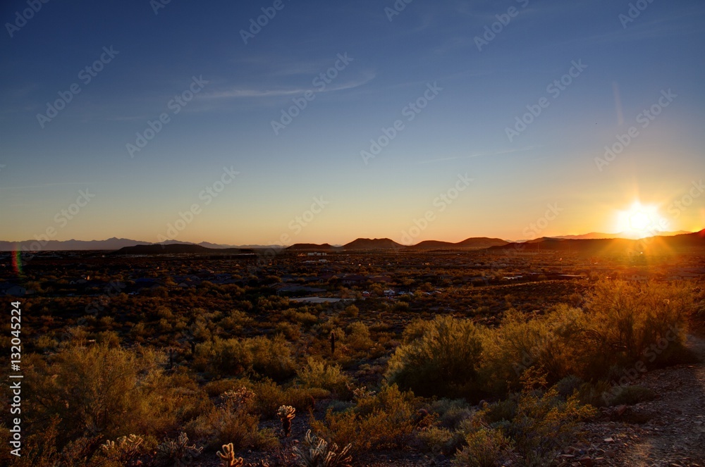Phoenix, Arizona -  The sun setting in the desert over mountains in the distance.