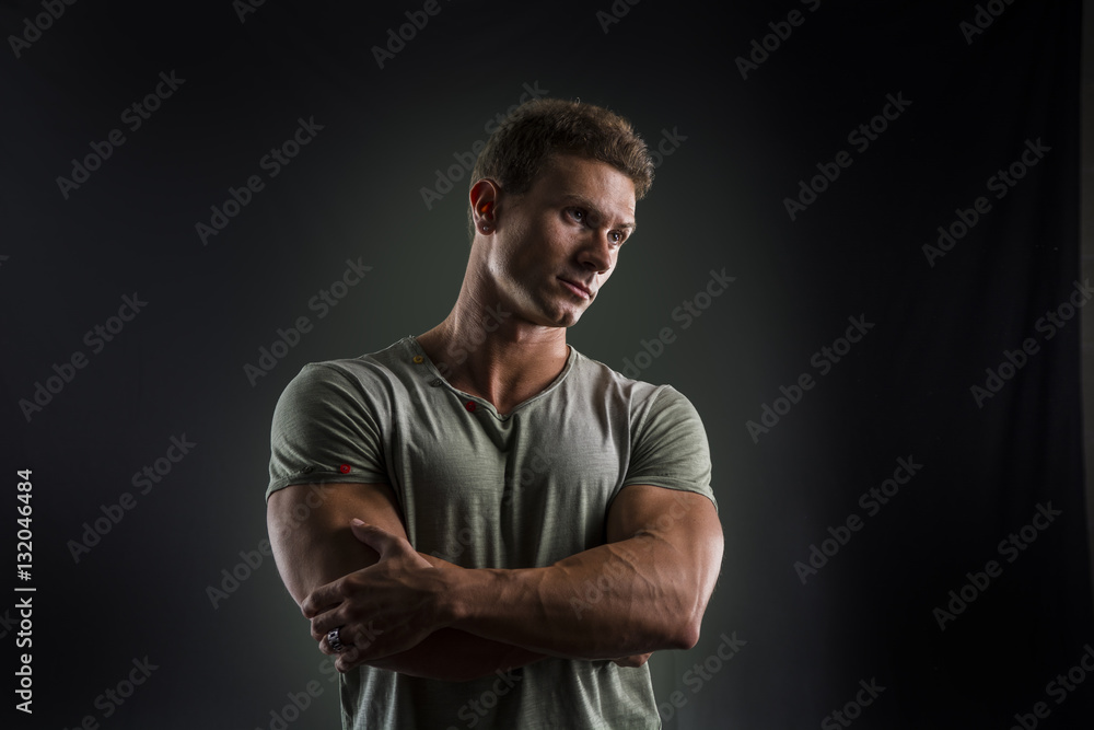 Fit handsome young man standing confident in casual clothes, looking down, arms crossed