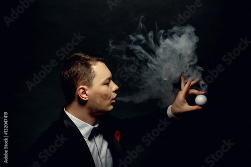 Fotografering Illusionist man makes smoke his hand on a dark background.