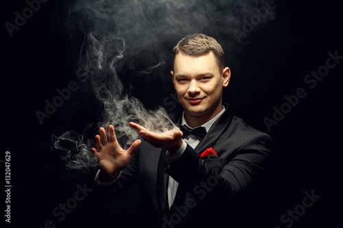 Illusionist man makes smoke his hand on a dark background. Fototapet