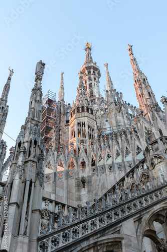Details of marble spiers and statues of Milan Cathedral, Italy, at sunset.