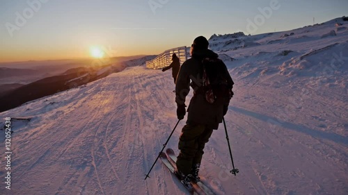 Slowmotion footage of a skier and snowboarder riding the slope during a beautiful sunset.