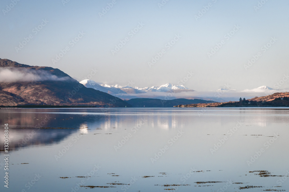 A calm winter landscape image of Loch Alsh with snowcapped Isle of Skye in the background