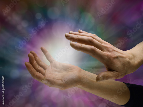 Sensing Paranormal activity - female hands sensing white energy  orb between hands on a dark multicolored bokeh background with copy space all around photo
