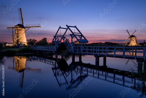 Fotografie Illuminated windmills, a bridge and a canal at sunset