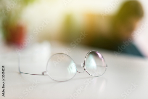 Elegant eyeglasses spectacles with thin titanium rim on office table with office employee silhouette working in the background