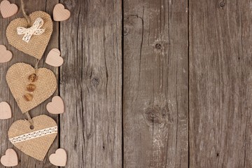 Side border of handmade burlap hearts with ribbon and buttons over a rustic wooden background