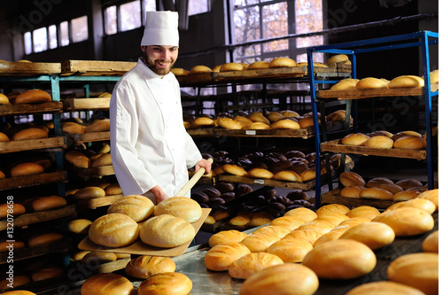 young handsome guy baker pulls out of the oven fresh bread at the bakery background photo