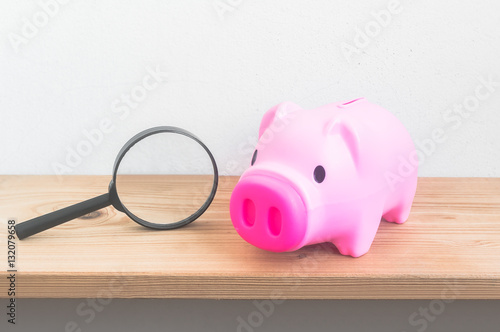 Piggy bank with magnifying glass on wooden shelf over grunge cem photo