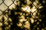 Abstract sun glowing behind a chain link fence close up