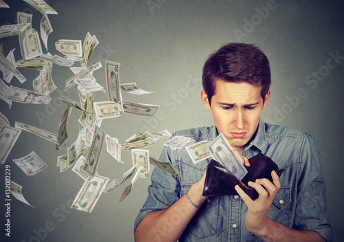 Sad man looking at wallet with money dollars flying away photo