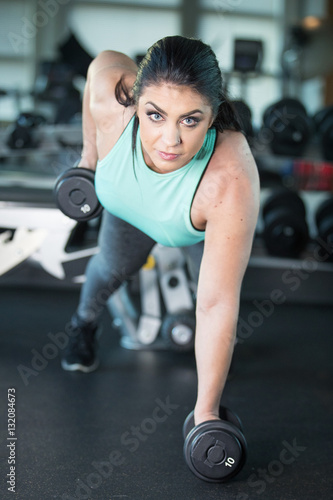 Pretty woman with blue eyes doing pushups with barbells in gym w