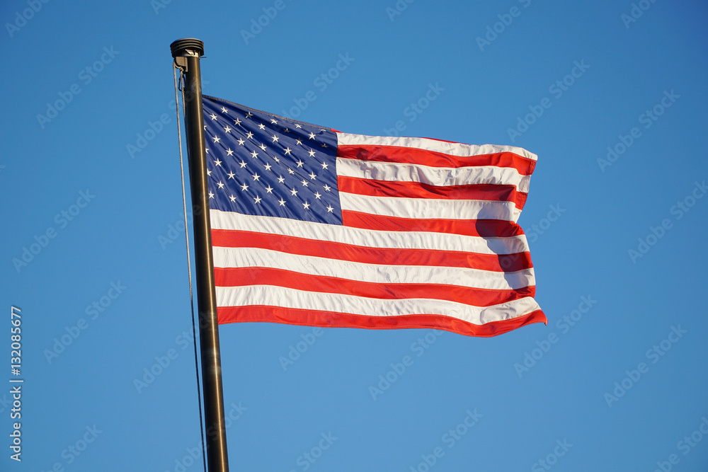 Obraz premium waving USA flag on pole against blue sky