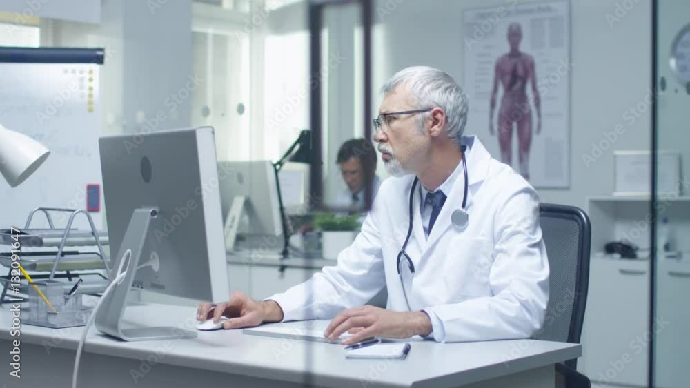 Senior Doctor and His Assistant Working at Desktop Computers. Sitting in Brightly Lit Office. Shot on RED Cinema Camera in 4K (UHD). Senior Doctor and His Assistant Working at Desktop Computers. Sitting in Brightly Lit Office. Shot on RED Cinema Camera in 4K (UHD).
