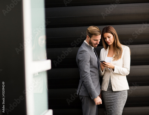 Young couple with mobile phone in front of office building