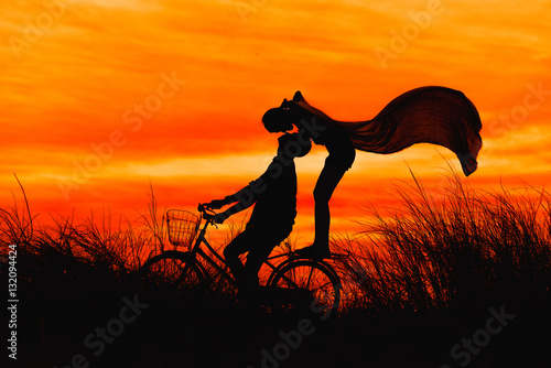 Silhouette couple kissing on bike over sunset background.