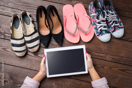 Female shoes collection on wooden table with woman's hands holding white digital tablet