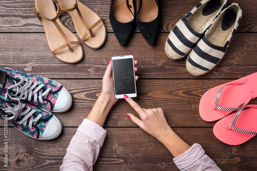 Female shoes collection on wooden table with woman's hands using smart phone