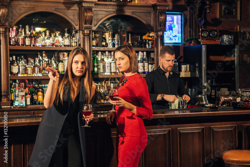 Two female friends are in the bar for a drink and talk. The woman with talks near the ear of the friend