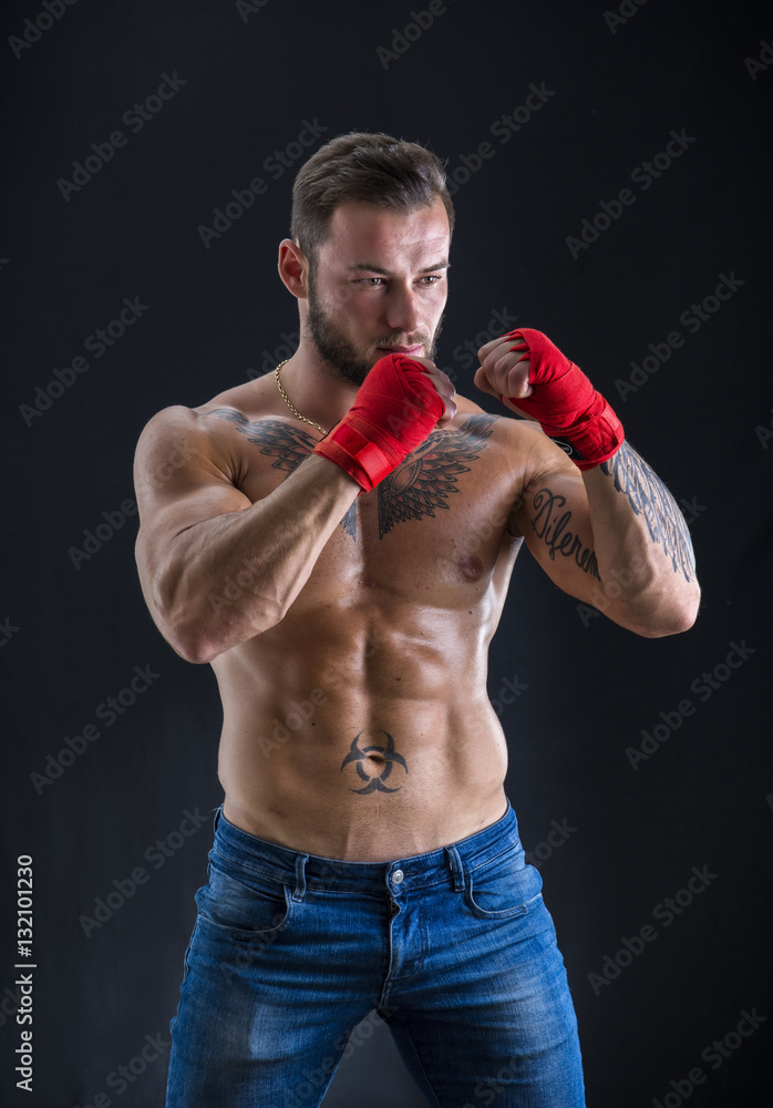 Young handsome topless boxer in red gloves looking at camera on black studio