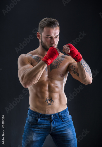 Young handsome topless boxer in red gloves looking at camera on black studio