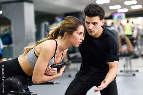 Slika na platnu Personal trainer helping young woman lift weights