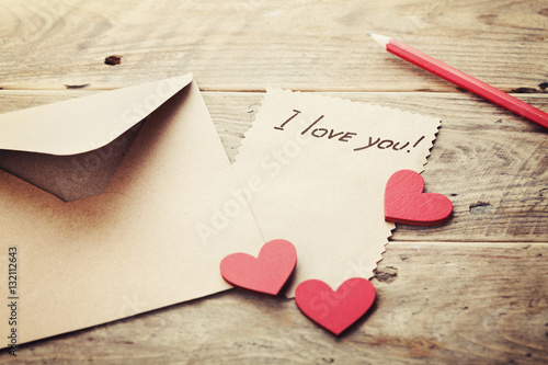 Envelope or letter, red hearts and notes I love you on vintage wooden table for Valentines Day in retro toning.