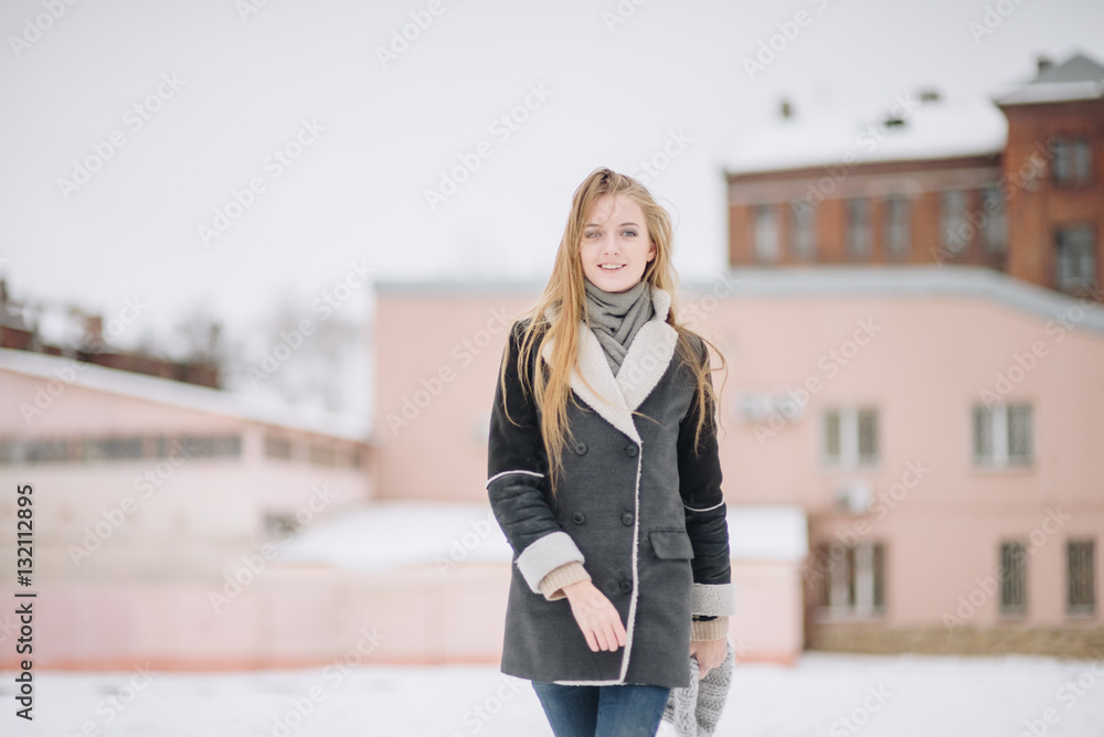 Young beautiful happy smiling girl posing on street. Model playing with her long hair, touching face. Woman wearing stylish clothes. Winter holidays concept. Magic snowfall effect