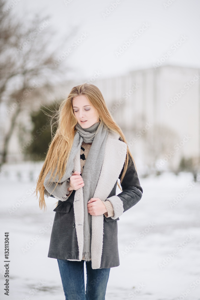 Young beautiful happy smiling girl posing on street. Model playing with her long hair, touching face. Woman wearing stylish clothes. Winter holidays concept. Magic snowfall effect