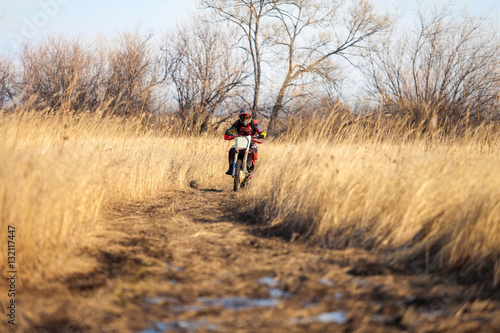 Enduro bike rider on a field with dry grass in autumn