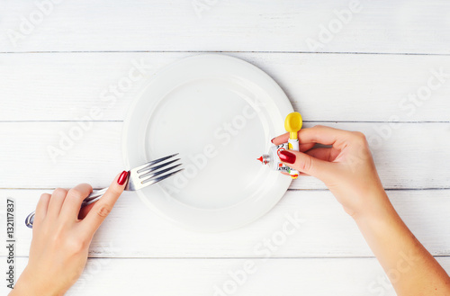 Concept photo: food from a tube. Not healthy, genetically modified food. Woman's hands push from the tube on a white plate at white wooden background. Preparing to eat food from the tube. photo