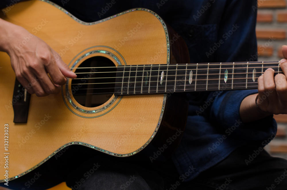 .A young man playing acoustic guitar happily in the music room.