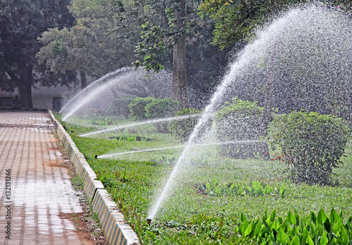 Several working water sprinklers in a row irrigating park garden