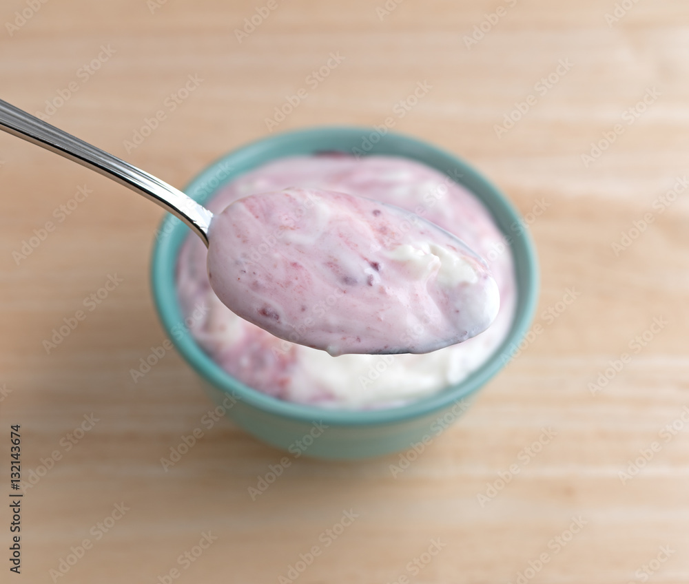 Raspberry yogurt on a spoon with bowl underneath atop a wood table. Raspberry yogurt on a spoon with bowl underneath atop a wood table.