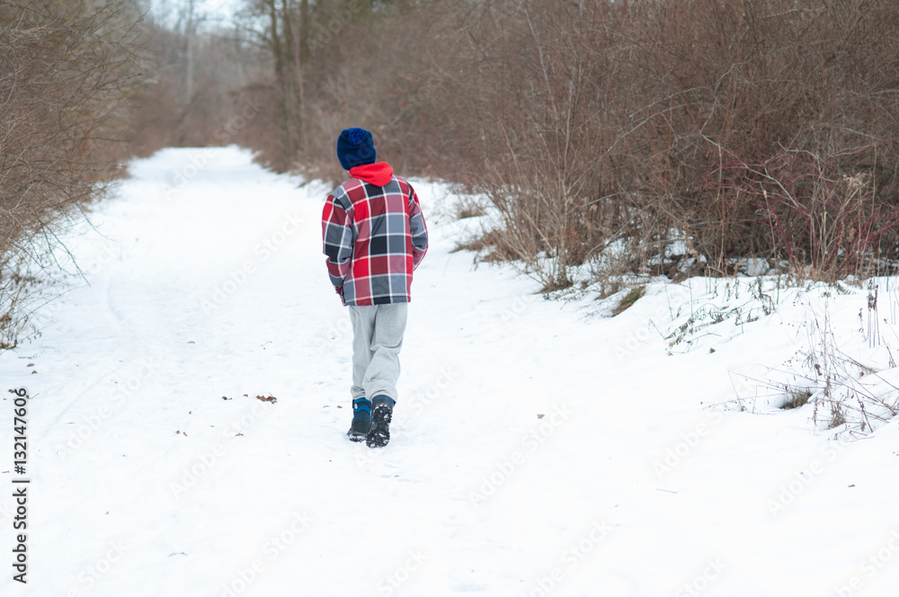 boy in winter wear walking down a snowy path
